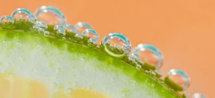 Dewdrops on a vibrant green lime slice against a soft orange background.